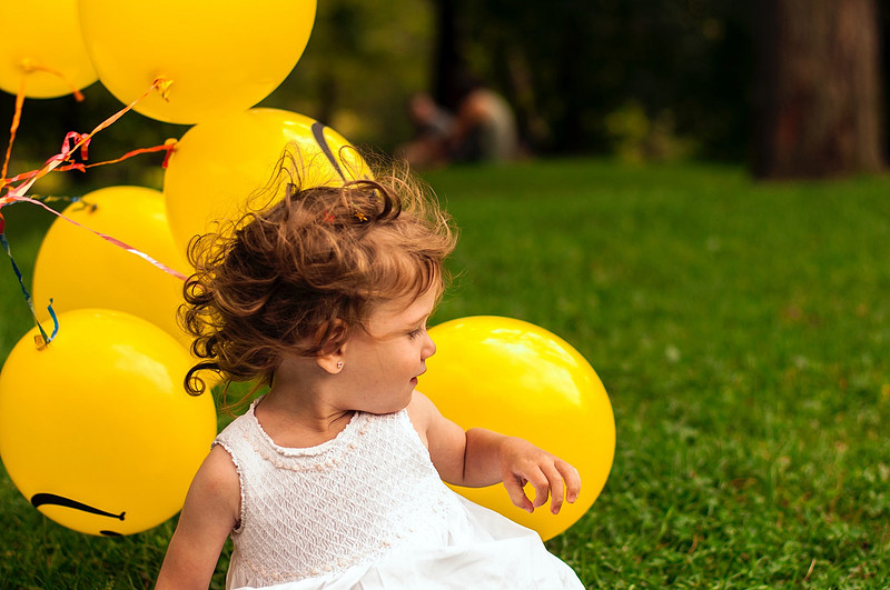 A young flower girl on the wedding day sitting on a field of grass with yellow balloons | Laura Mares Photography | Pittsburgh Photographer